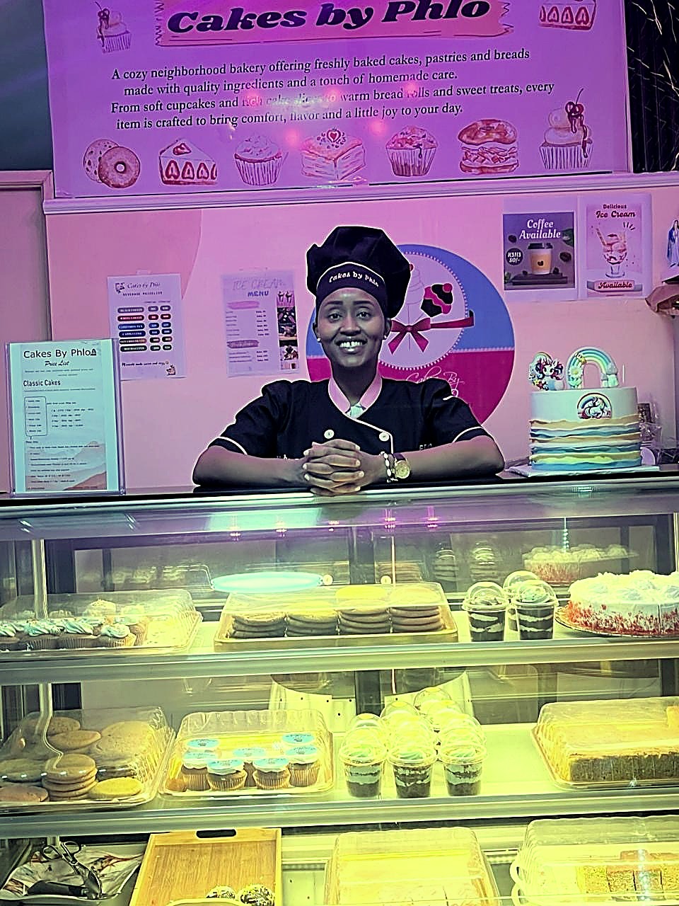Phlo, founder of Cakes by Phlo, smiling behind the bakery display case in Buruburu